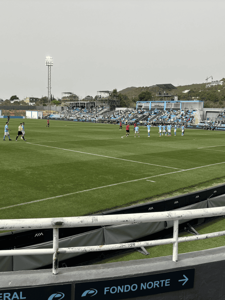 Soccer stadium with players, fans, and scenic hillside background | QuestForDirections.