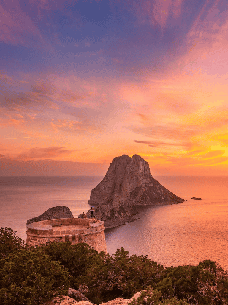Cliffs of Es Vedrà near Ibiza during sunset against colorful sky.