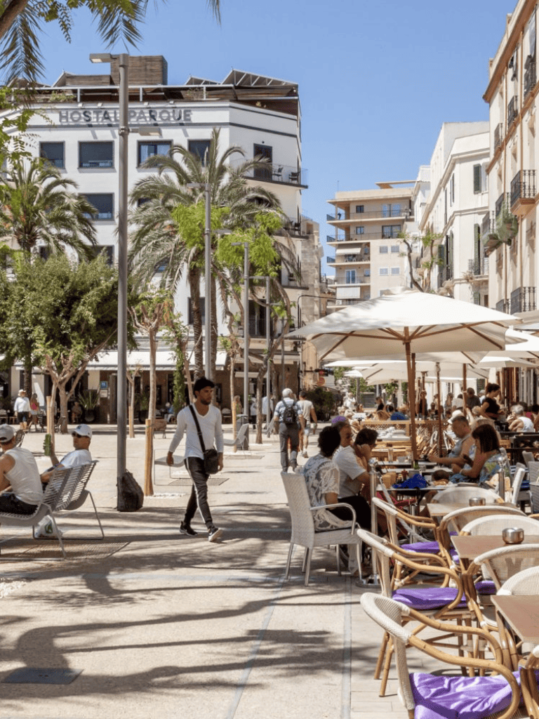 Outdoor dining in a lively city street with palm trees and modern buildings, sunny day, tourists enjoying meals and cafes.