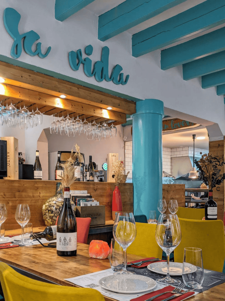 La vida restaurant interior with vibrant decor, wine bottles, and glasses set for dining, highlighting a cozy, elegant atmosphere.