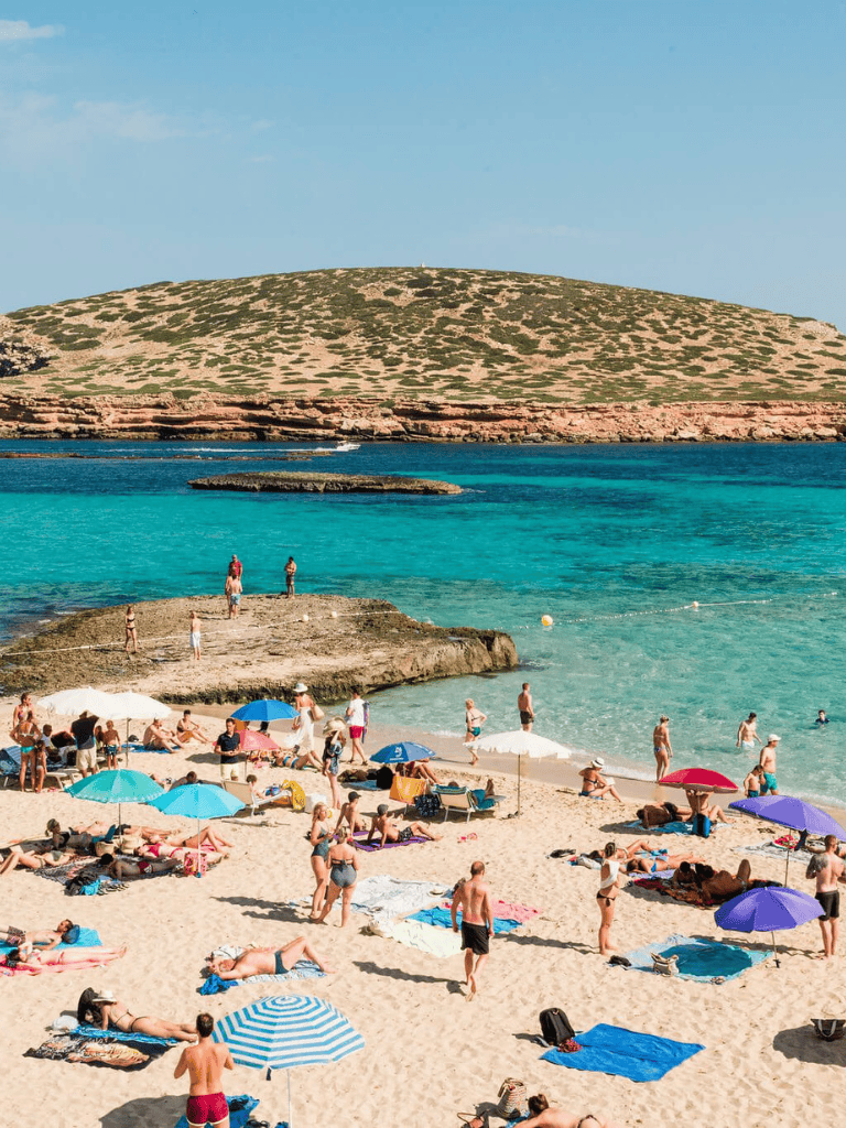 Relaxing beach scene with colorful umbrellas, sunbathers, and turquoise waters at a popular tourist destination.