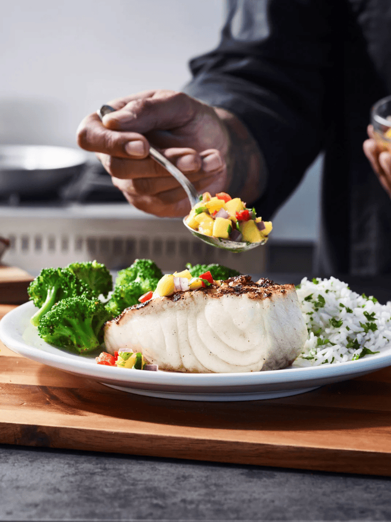 Succulent fish dish with broccoli, rice, and fresh vegetables garnished for a healthy meal.