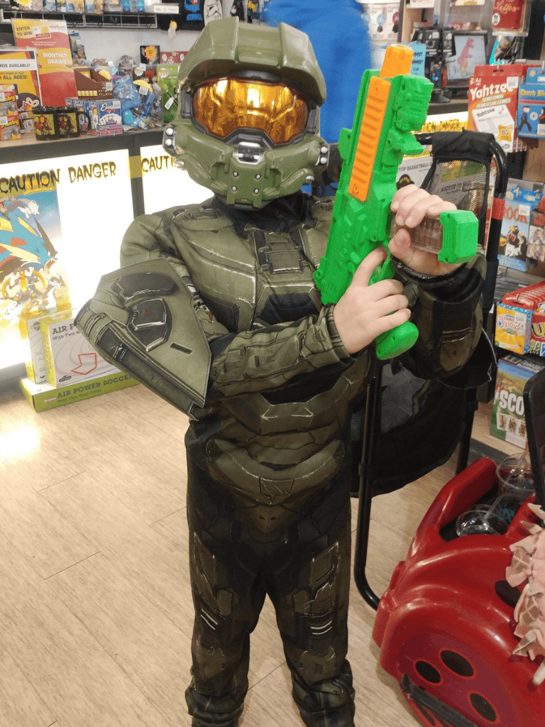 Kids dressed as Master Chief from Halo holding toy gun in toy store aisle.