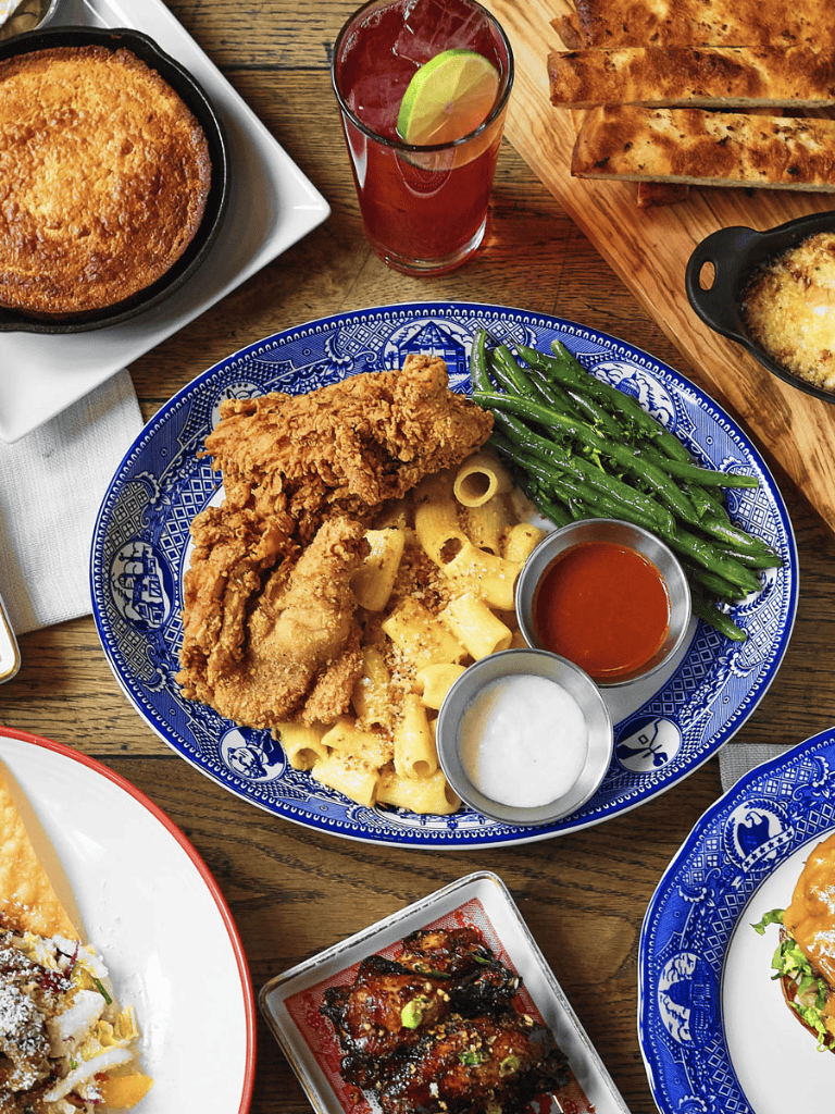 Crispy fried chicken with green beans, pasta, and dipping sauces on a blue plate at a restaurant.