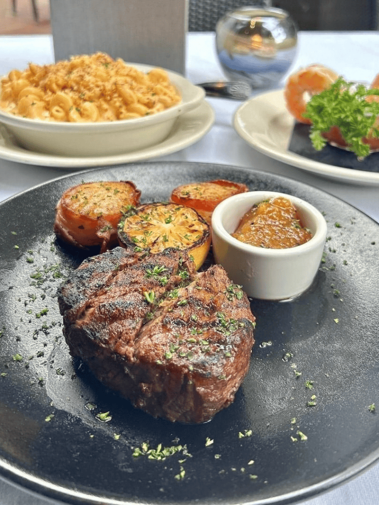 Juicy grilled steak with roasted tomatoes and savory sauce on a black plate.