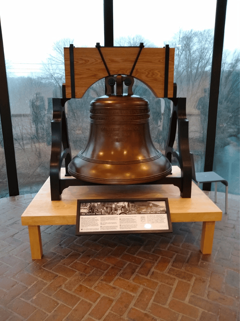 Large bronze liberty bell on display at a museum with an informational plaque in front.