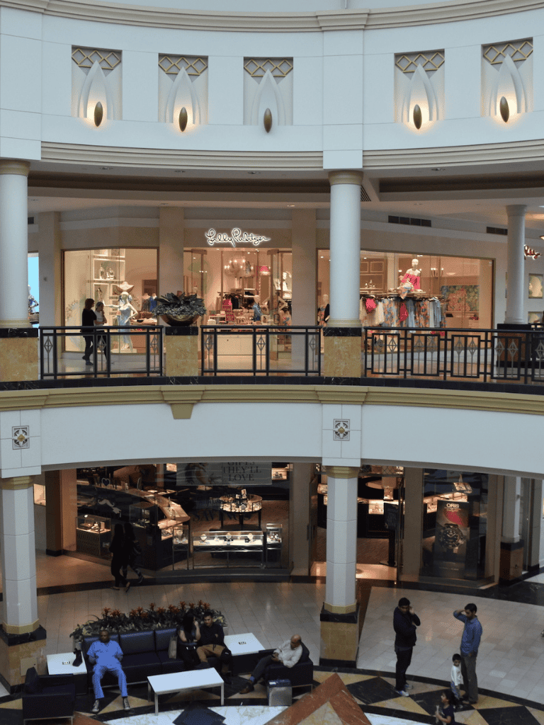 Elegant shopping mall with luxury boutiques and shoppers, modern architecture with stylish decor.