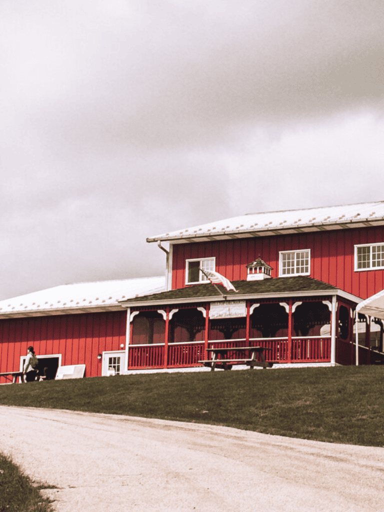 Vintage red barn with white accents and snow-covered roof, accessible by a sloped driveway.