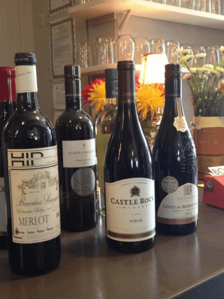 Rich red wine bottles at a cozy wine bar with flowers and warm lighting.