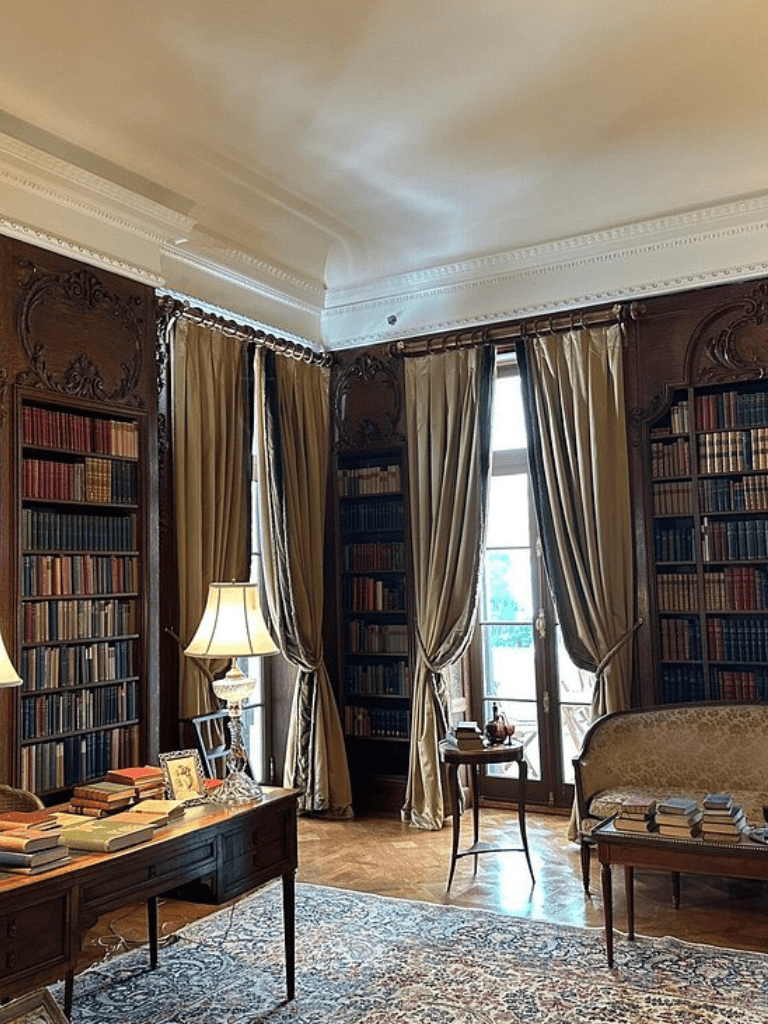 Cozy historic library with wooden shelves, plush seating, and large windows for reading and study.