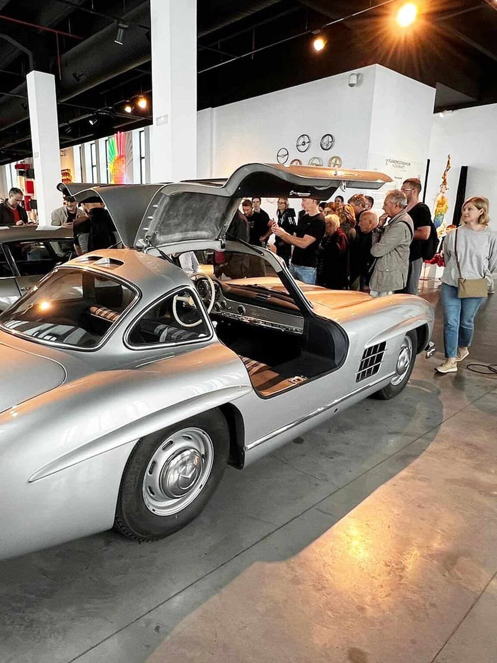 Vintage silver sports car at an automobile museum with visitors observing.