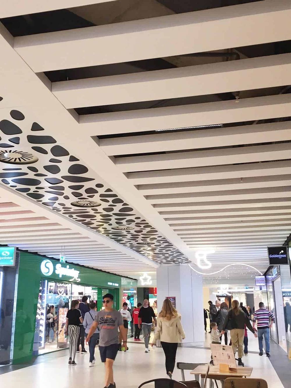 Bright modern shopping mall interior with ceiling design and diverse shoppers.