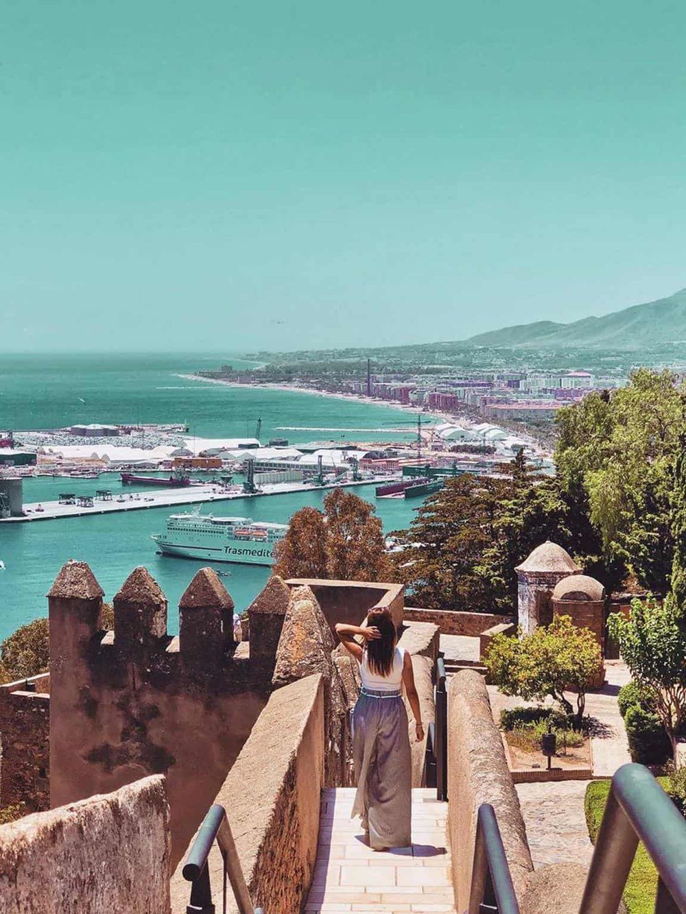 Scenic coastal view from historic site with woman overlooking the harbor and cityscape.