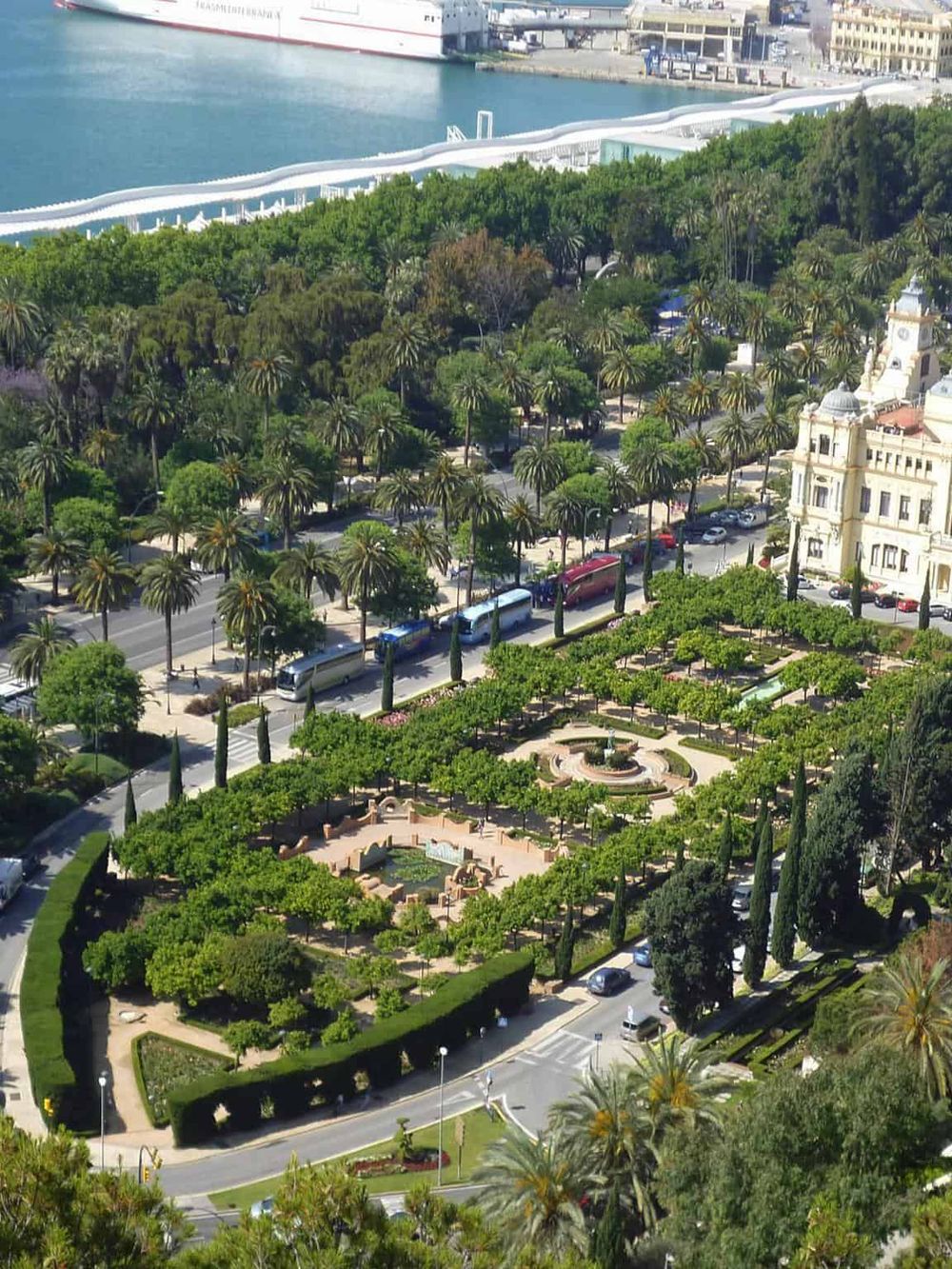 Lush green park with palm trees by the waterfront in Monaco, featuring a fountain and surrounding historic architecture.