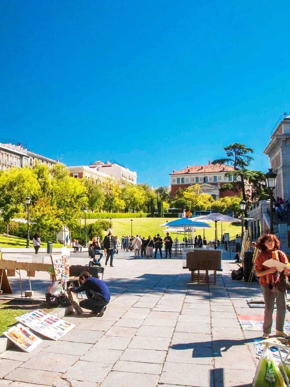 Colorful outdoor marketplace with art vendors and lush greenery under a bright blue sky.