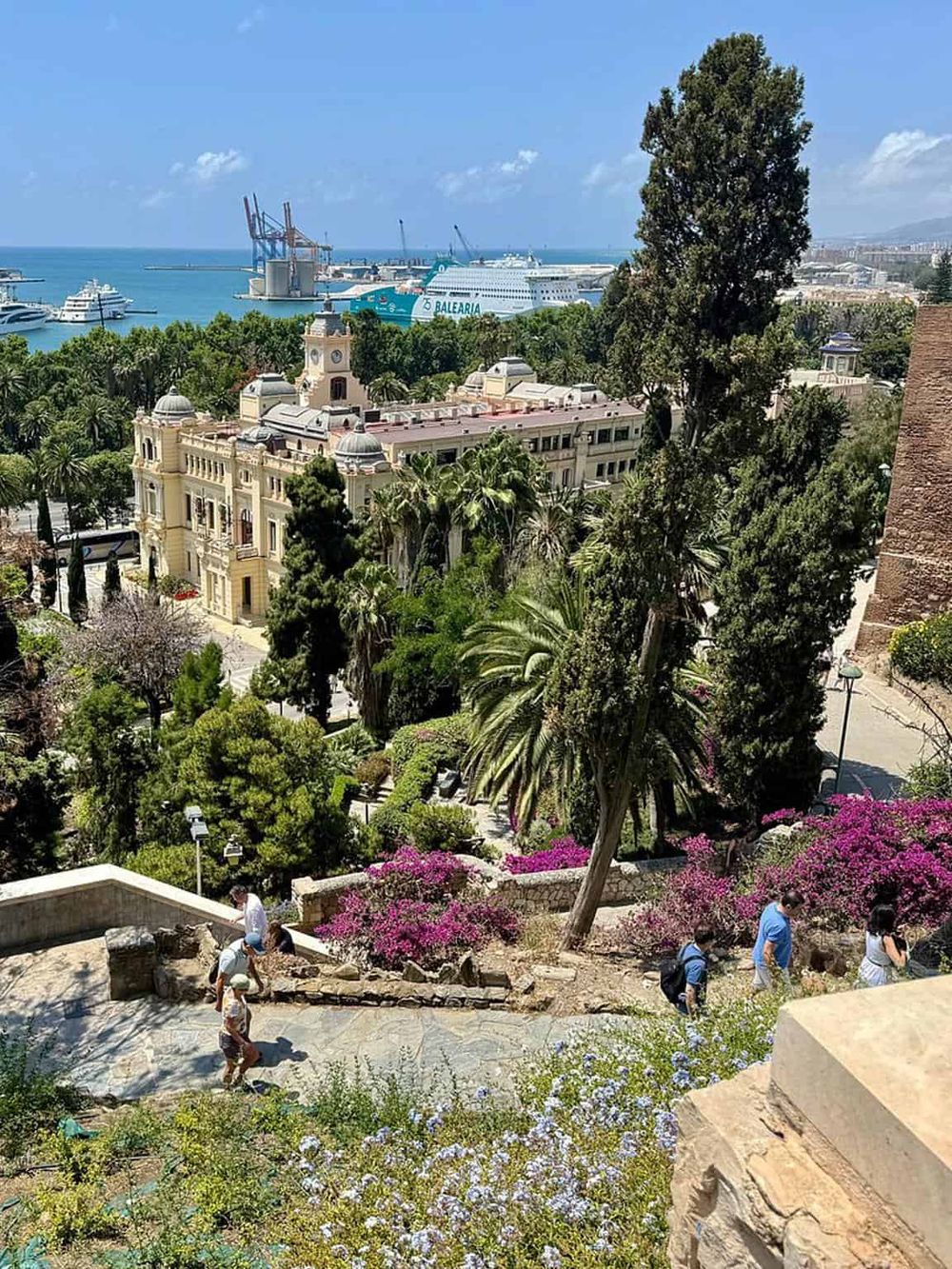 Panoramic view of lush gardens and historic architecture overlooking the port of Palma de Mallorca, with cruise ships in the distance.