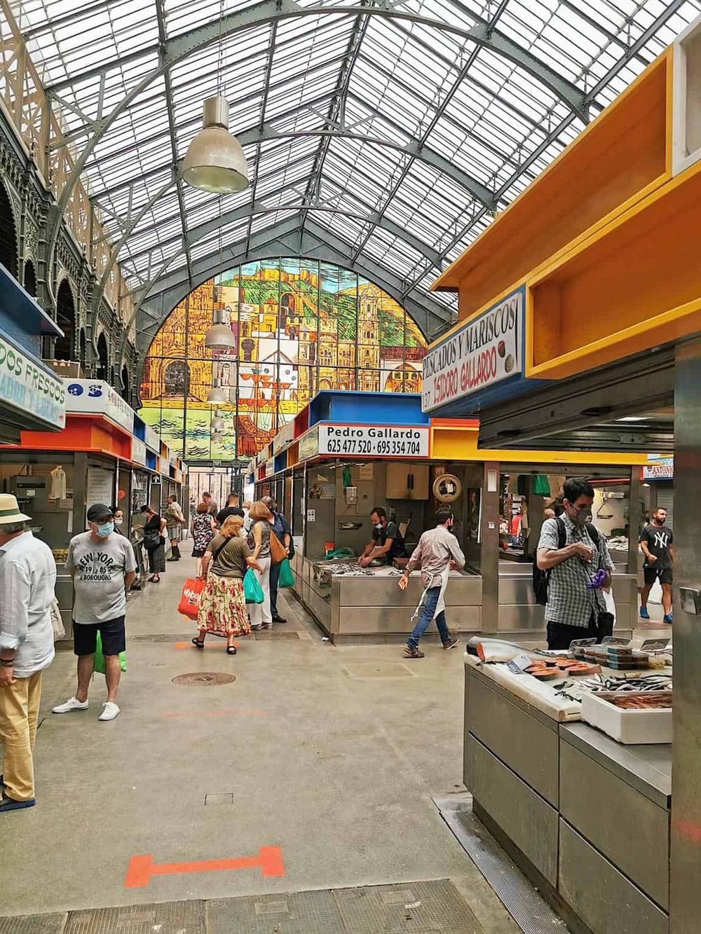 Colorful indoor market with seafood vendors, shoppers, and a stained glass ceiling.