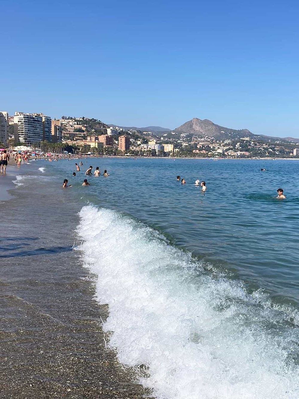 Beach scene with people swimming and relaxing by the shoreline in a popular Mediterranean coastal destination.