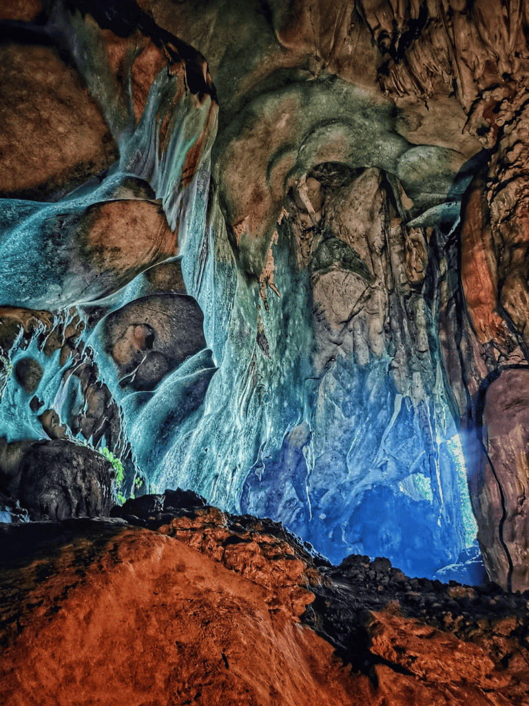 Vivid underground cave with flowing water and colorful stalactites and stalagmites.