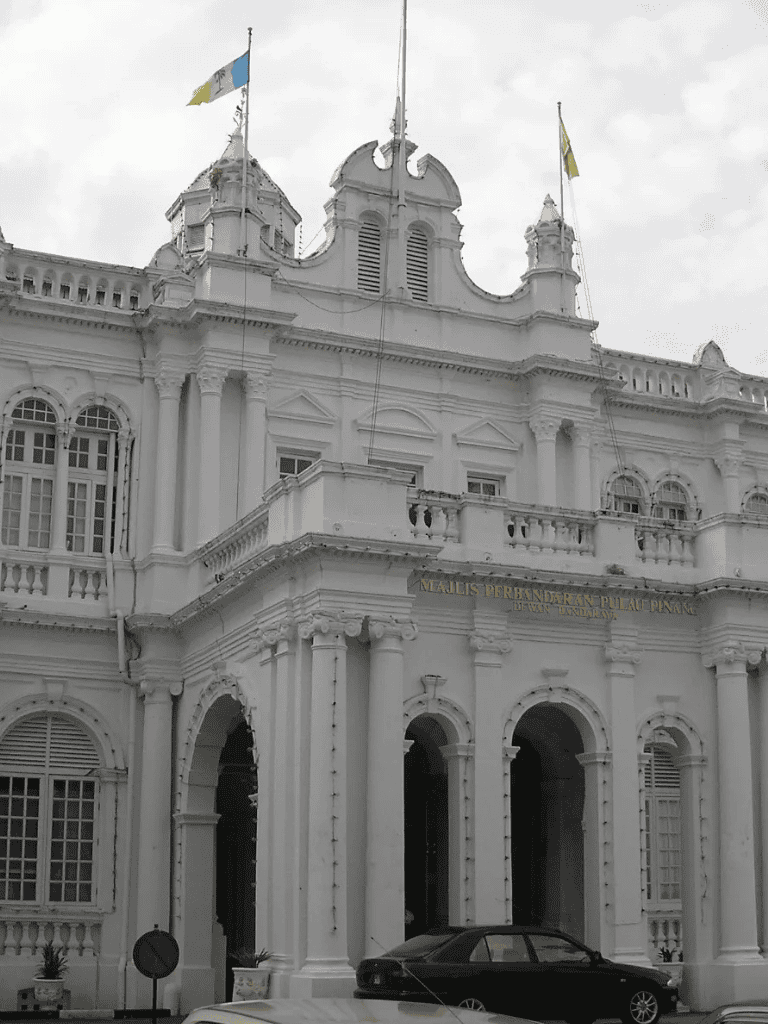 Grand historic white colonial building with flags, ornate architecture, and a black car in front.