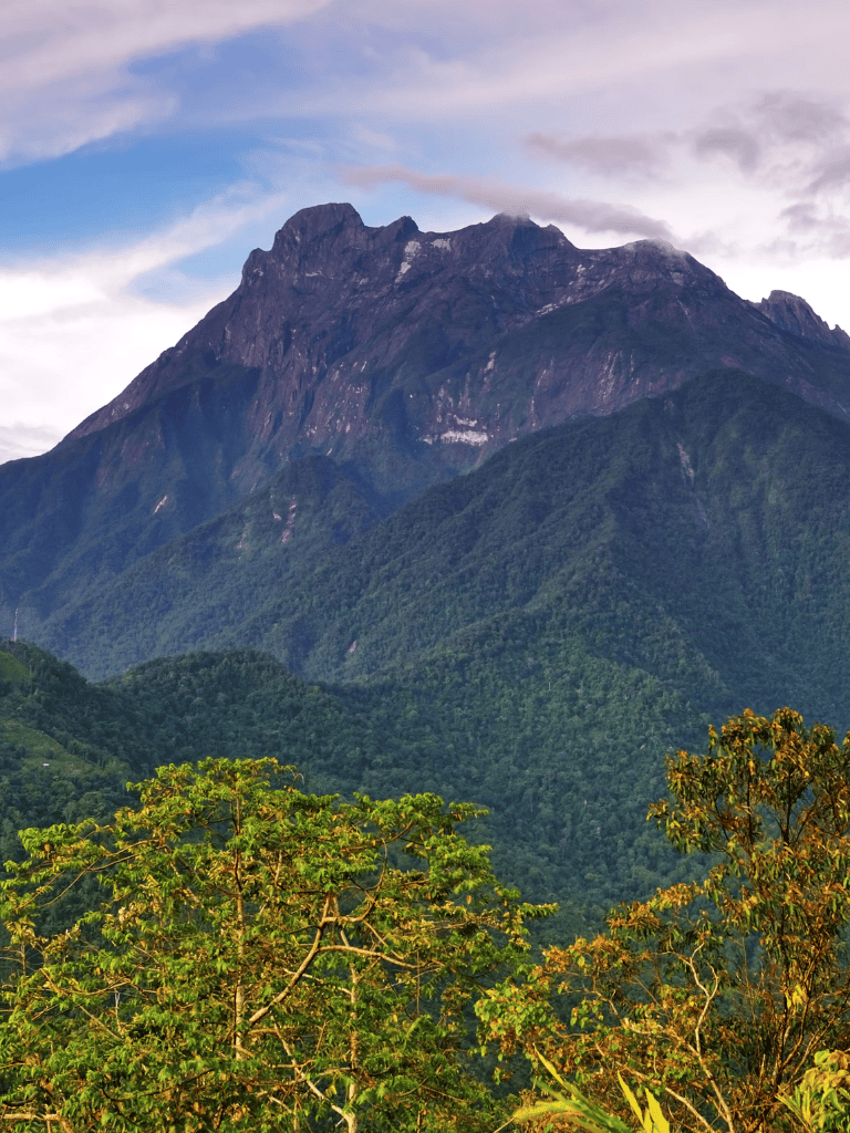 Lush green mountain landscape with towering peaks and vibrant forest in the foreground.