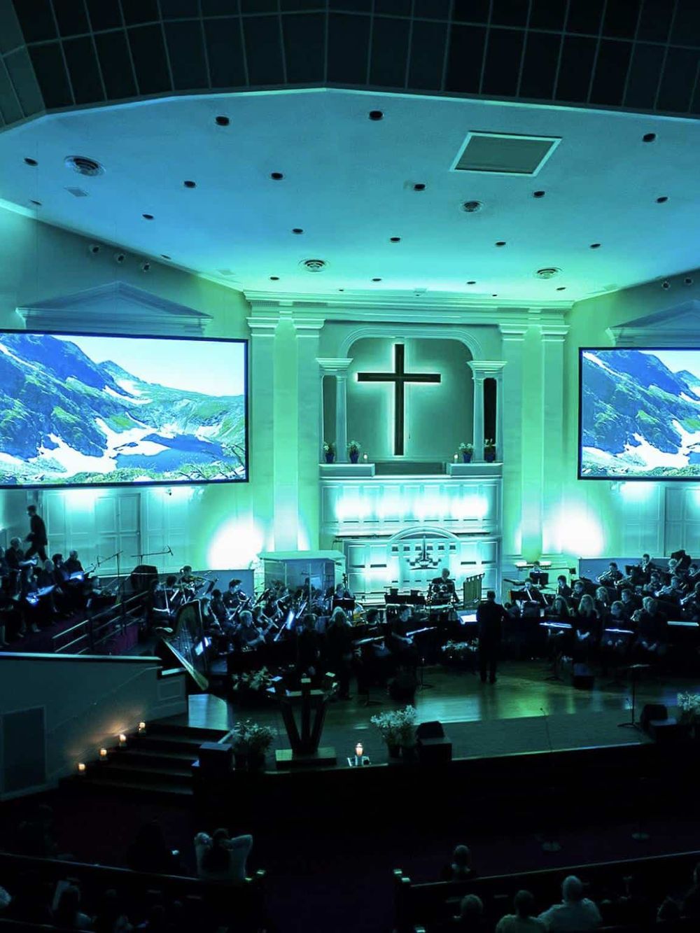 Serene church interior with illuminated cross and large screens displaying mountain scenery, ideal for spiritual gatherings and worship.