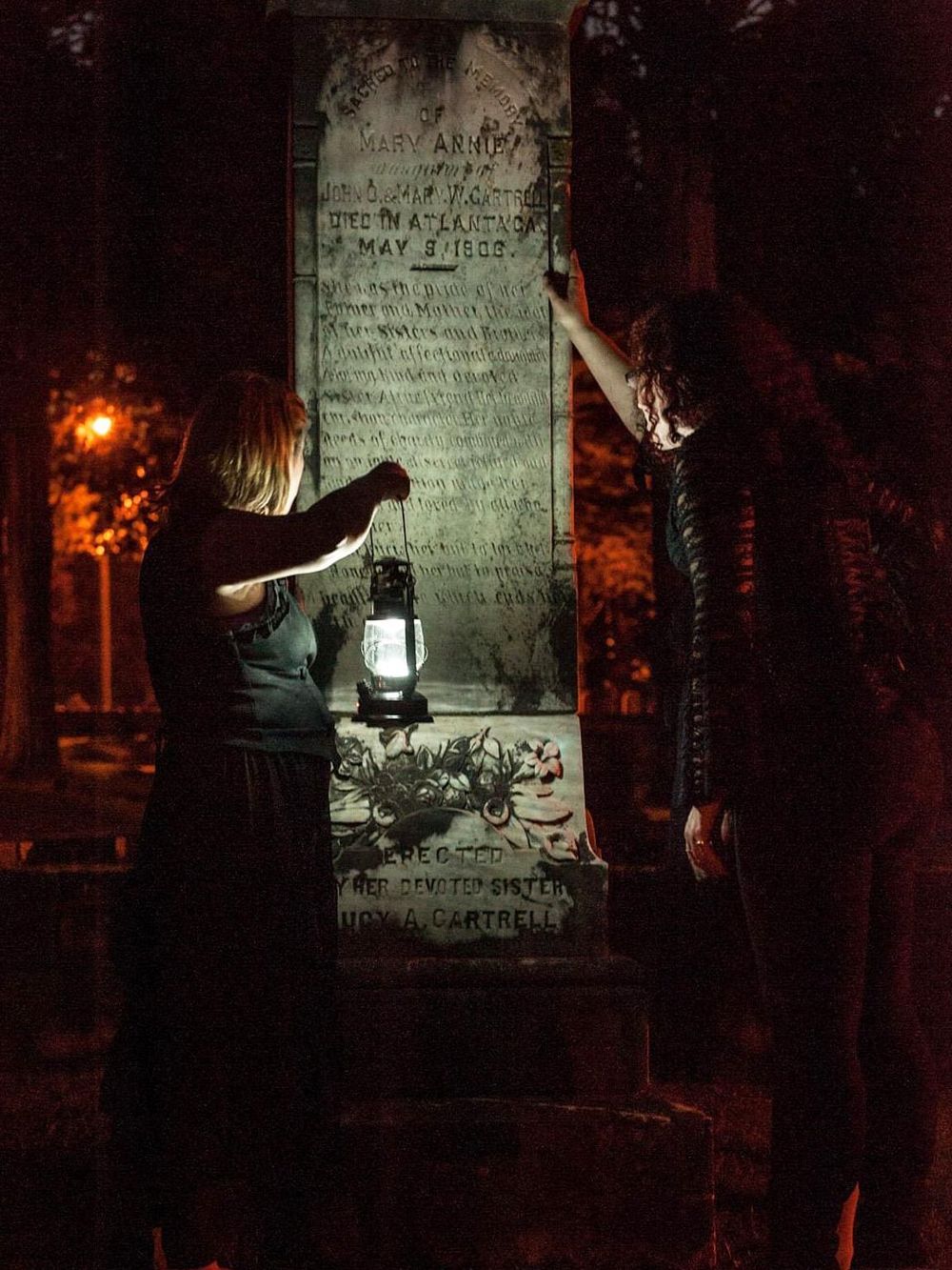 Historical monument at night with two women illuminating the plaque with a lantern.