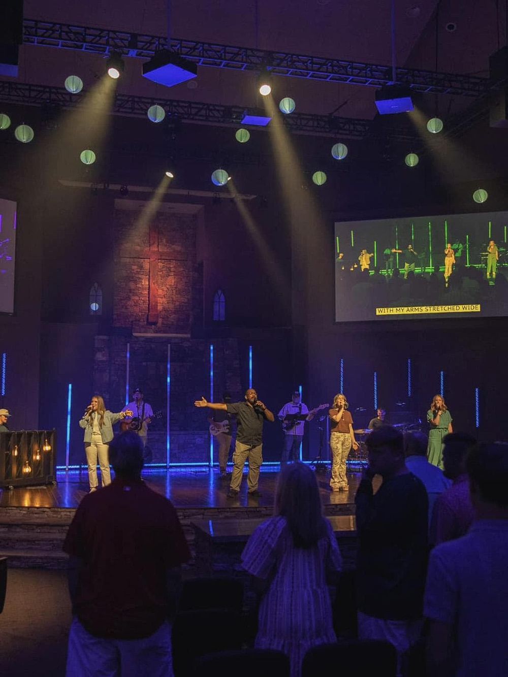 Vibrant church worship service with stage band, singers, and colorful lights in a modern sanctuary setting.