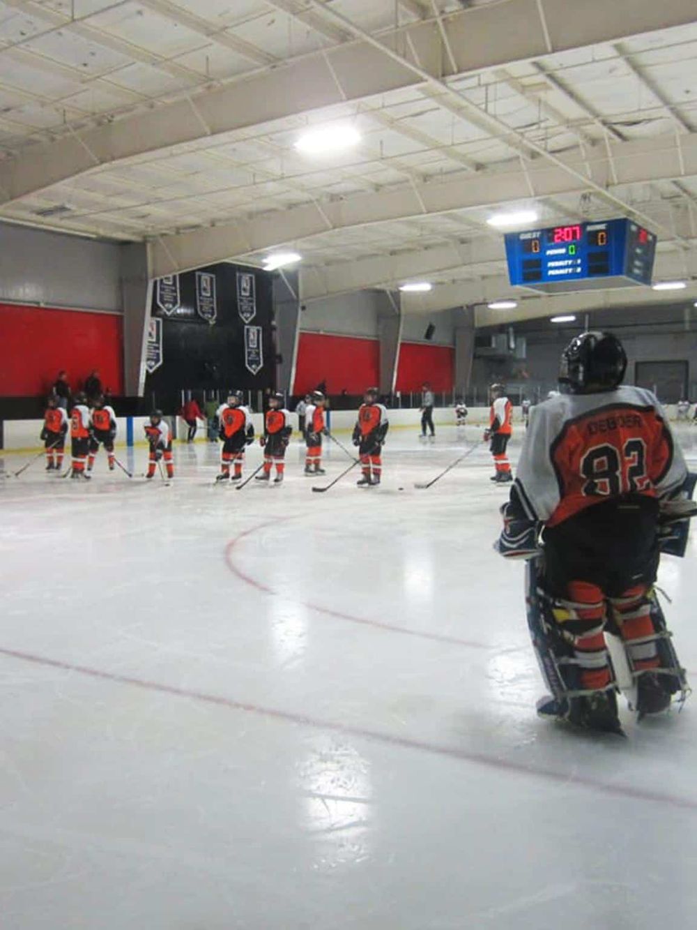 Ice hockey team practicing at indoor rink with scoreboard and players in action.