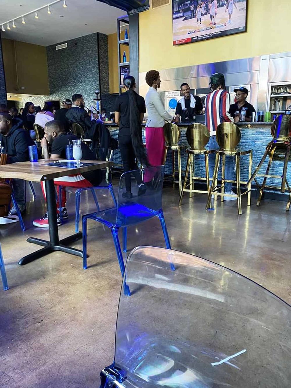 Modern sports bar with diverse patrons enjoying food and drinks, featuring large TV screens and vibrant interior decor.