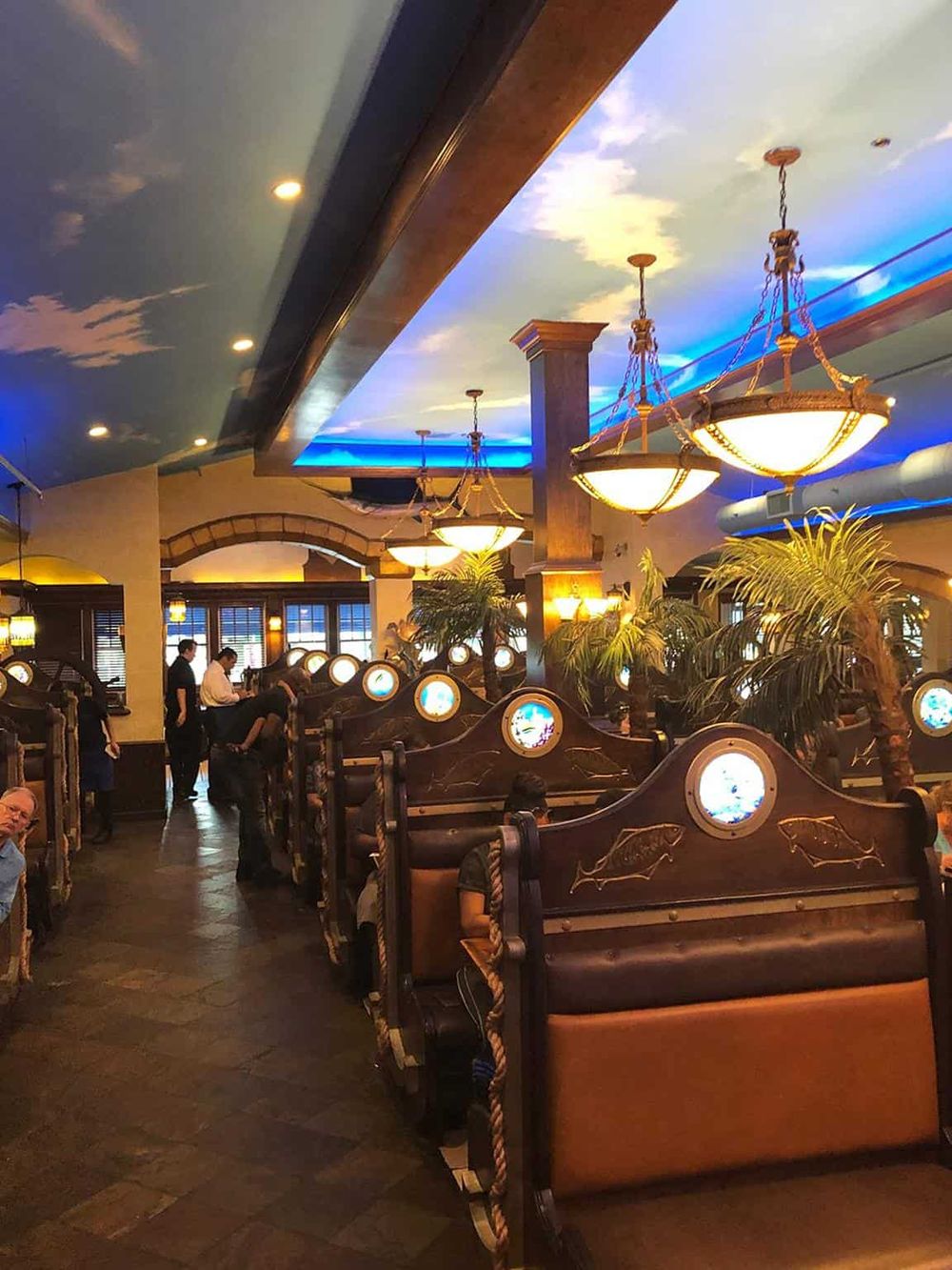 Vast indoor restaurant with tropical decor, wooden booths, and sky-themed ceiling lighting creating a relaxing ambiance.