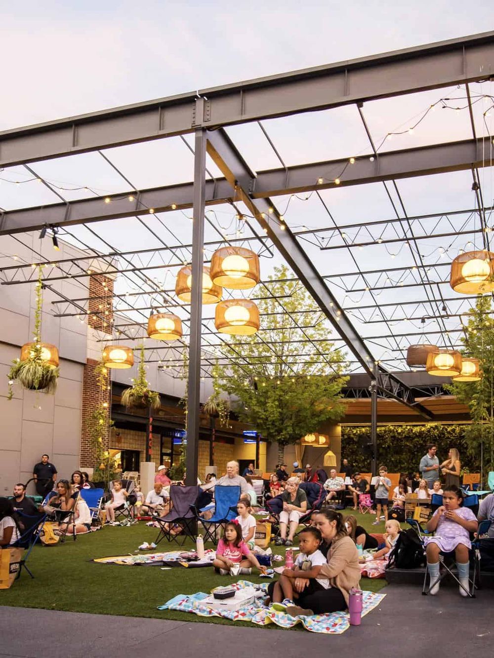 Outdoor community event with families under string lights and lanterns.