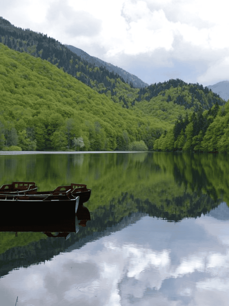 Tranquil lake surrounded by lush green mountains with boats in foreground, reflecting peaceful natural scenery.