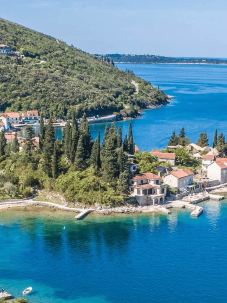 Stunning coastal view of lush green hillside, tranquil blue water, and charming seaside homes for travel inspiration.