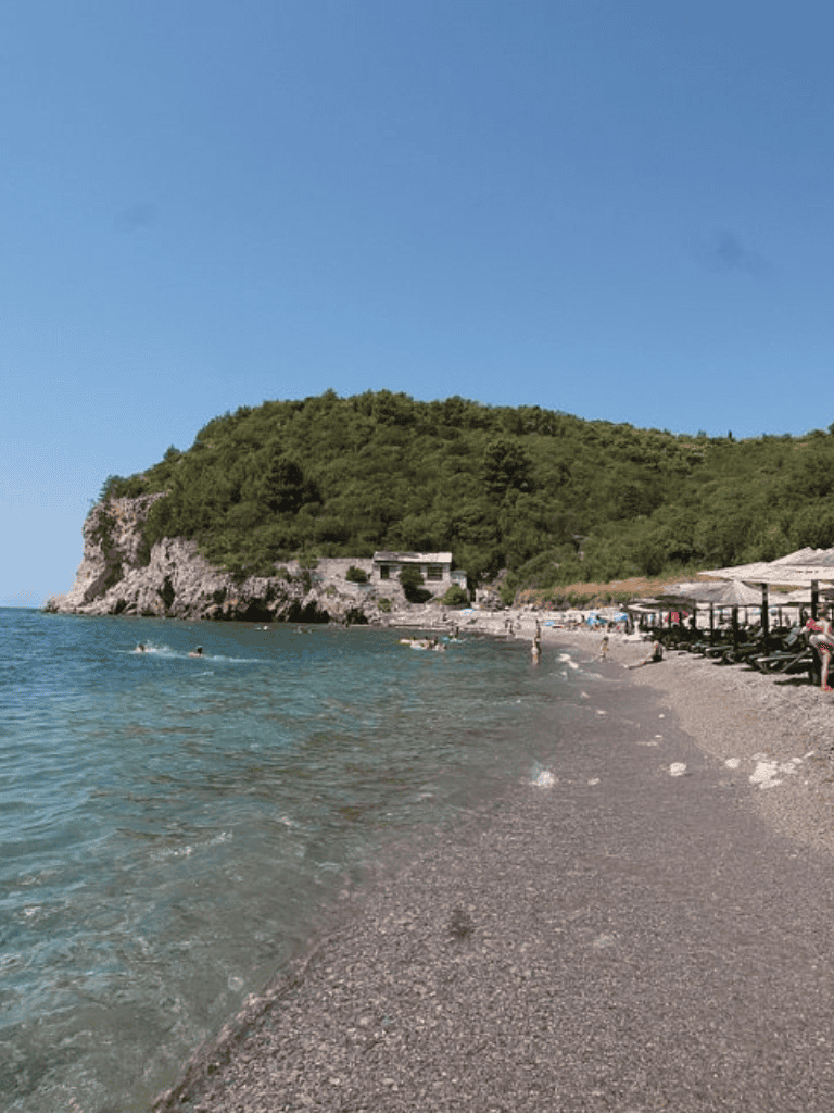Relaxing beach with clear waters and green hillside in the background, ideal for seaside vacations.