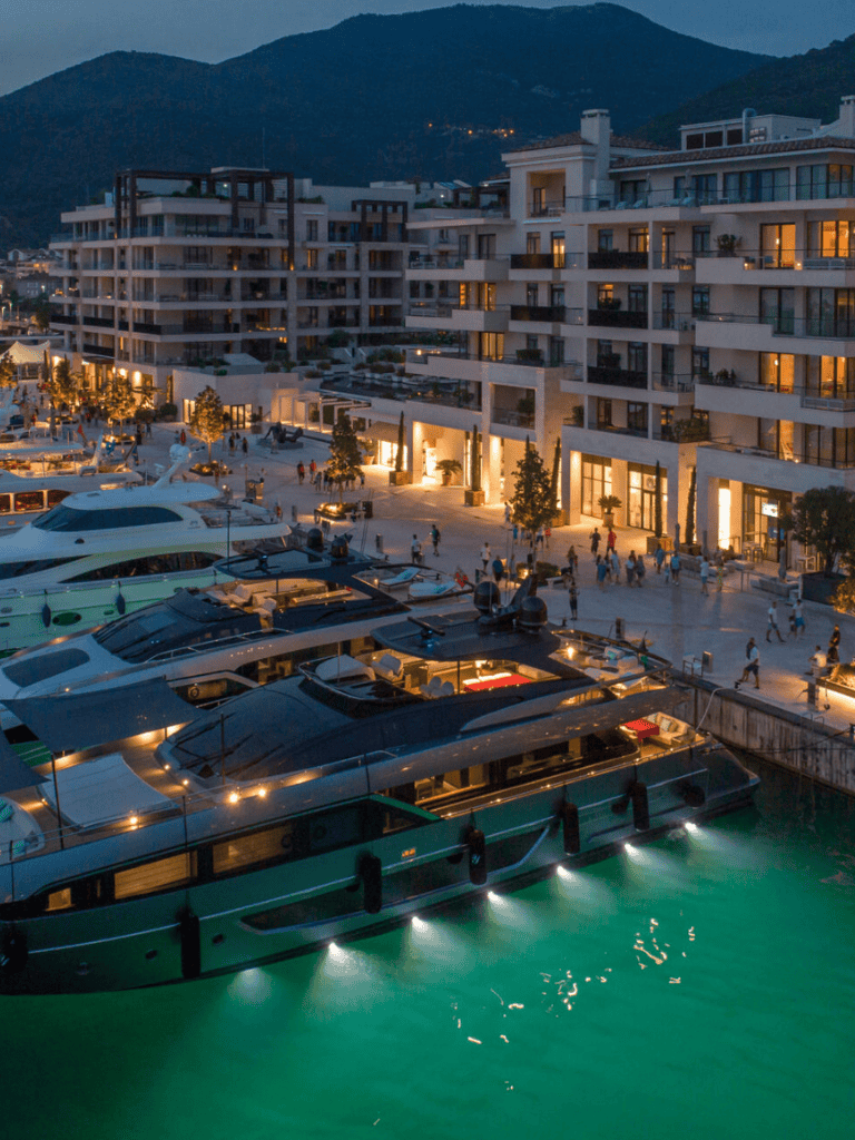 Luxurious waterfront apartment with yachts, mountain view, evening lights, vibrant marina scene.