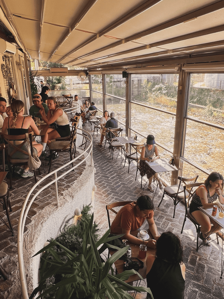 Cozy indoor café with large windows, diverse group of patrons, casual atmosphere, perfect for relaxing and socializing.