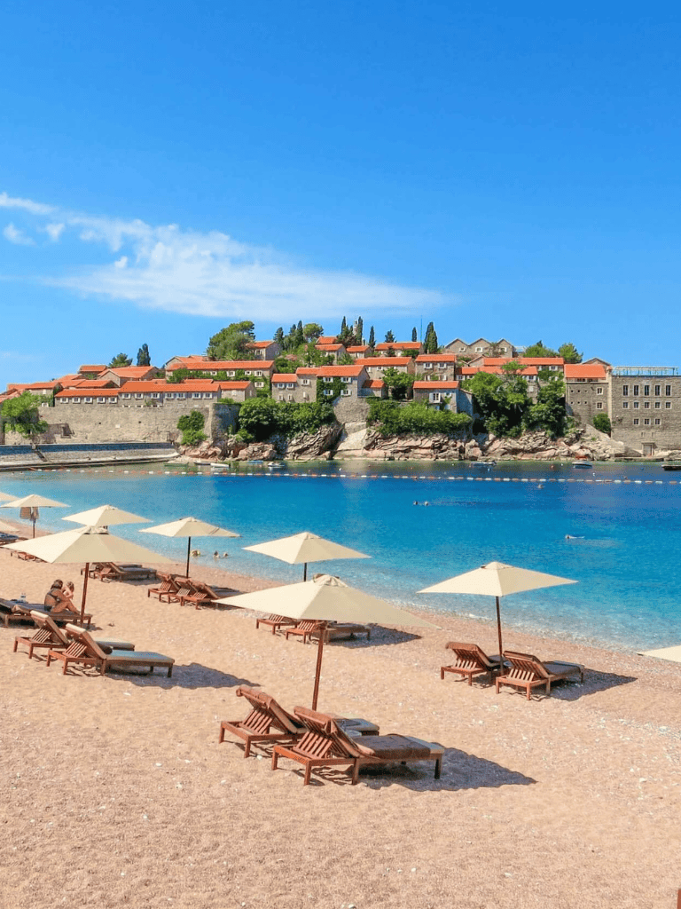 Beach with umbrellas and a historic hillside town in the background, perfect for travel destination search.