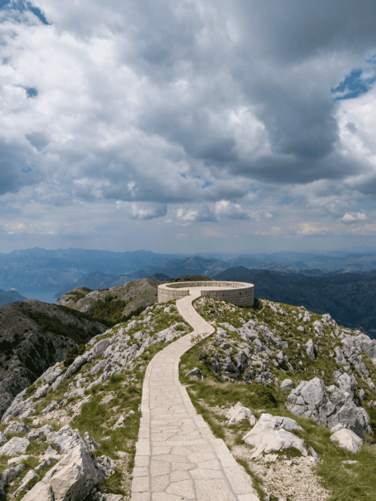 Stone mountain top viewing area with scenic mountain landscape and cloudy sky.