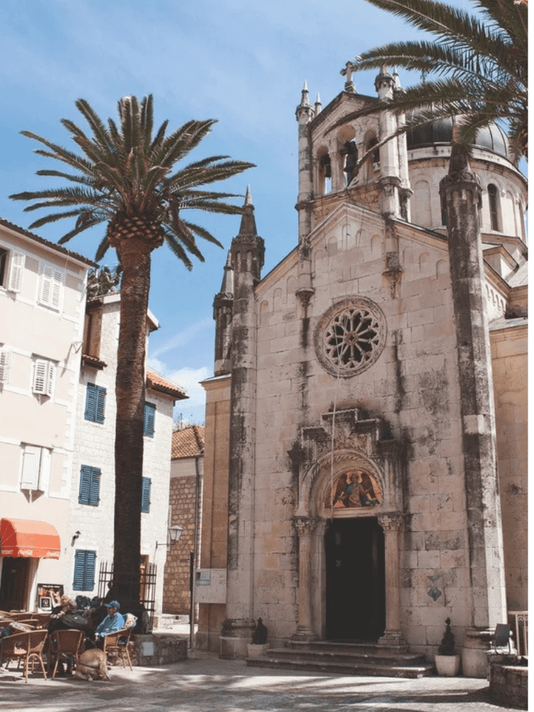 Historic church with palm trees in a Mediterranean town, featuring stone architecture and outdoor seating.