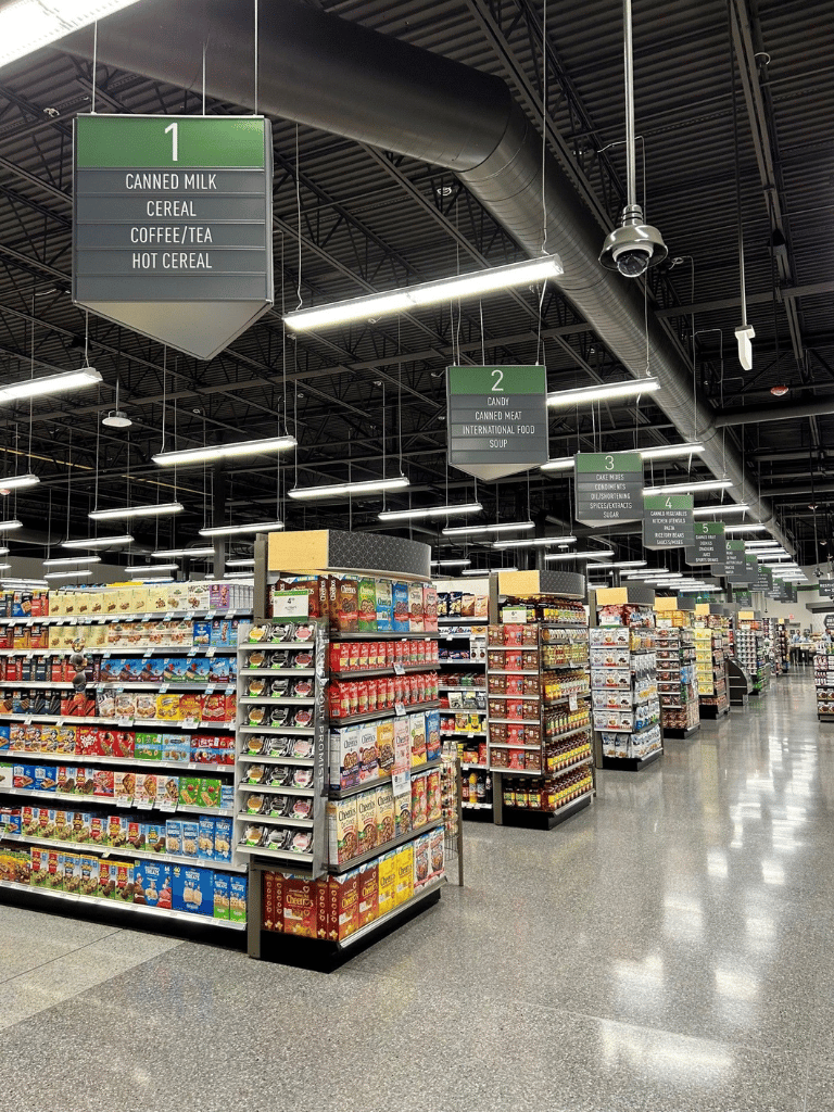 Canned milk, cereal, coffee/tea, hot cereal aisle in a grocery store with clear signage for directions.