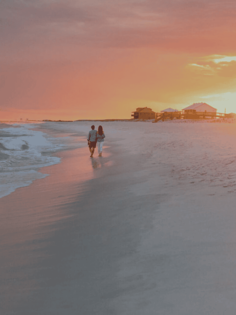 Sunset beach scene with couple walking along shoreline, tropical overwater bungalows in background, tranquil ocean setting, travel and vacation destination.