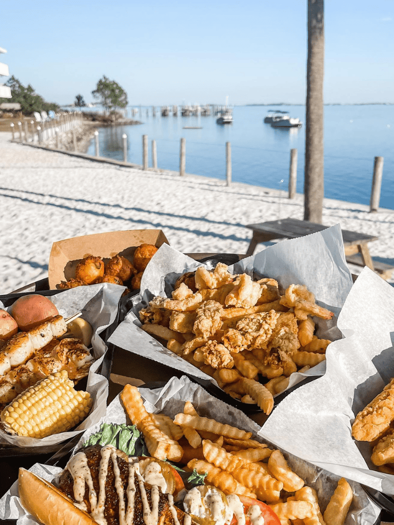 Crispy fried seafood platter with fries and corn on seaside dining table, waterfront view, and boat harbor.