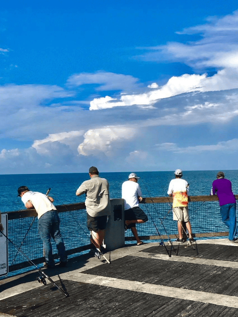 People fishing off a pier on a sunny day with blue skies and ocean scenery, promoting outdoor recreation.