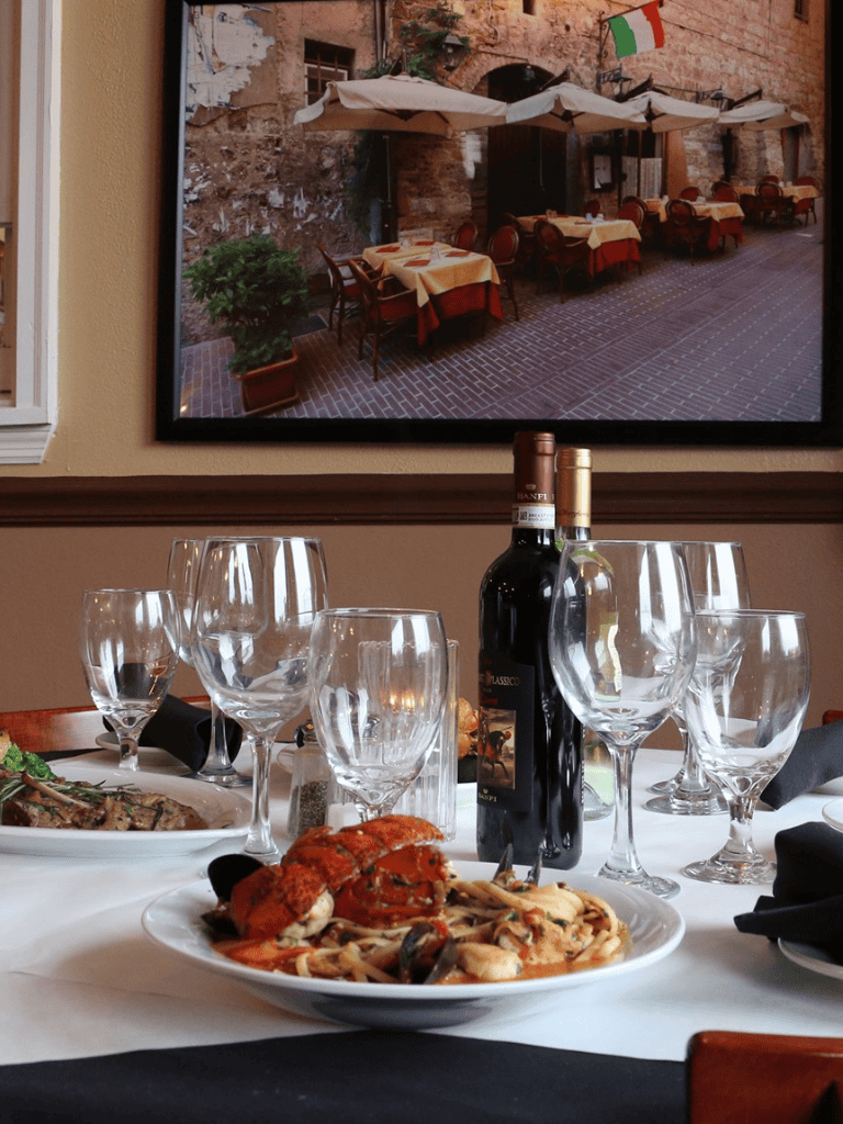 Elegant restaurant table setting with seafood dish and wine bottles, cozy Italian dining ambiance.