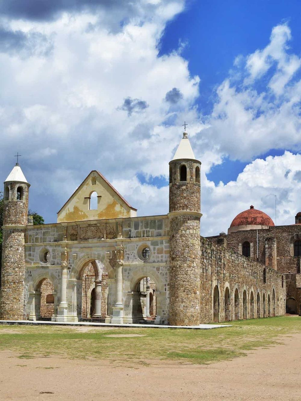 Ancient mission church with stone walls and bell towers against blue sky and clouds.