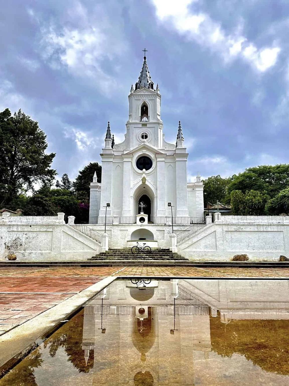 Historic white church with tall steeple and reflection in front, popular travel destination for tourists.