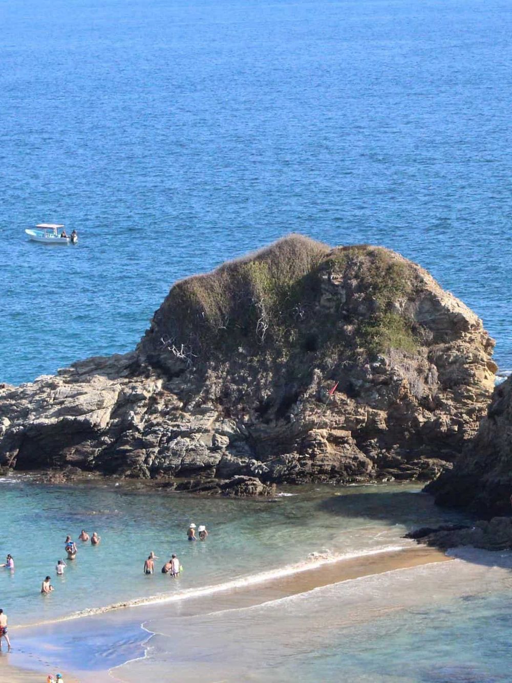 Secluded coastal cove with rocky formations, clear blue water, and visitors enjoying the beach.