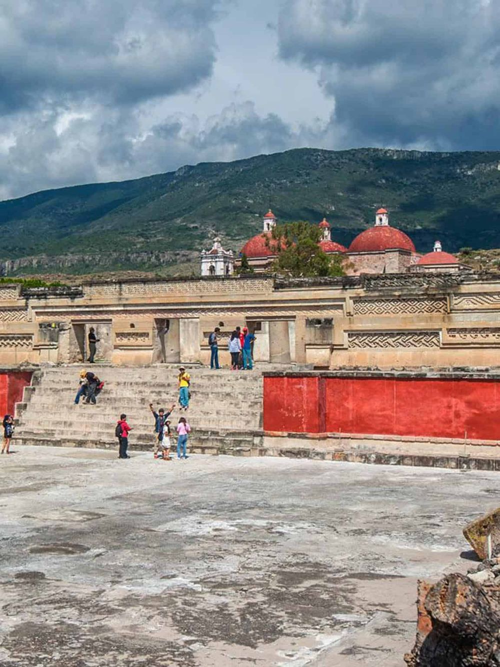 Colorful historical site with tourists exploring, set against lush mountains and cloudy sky.