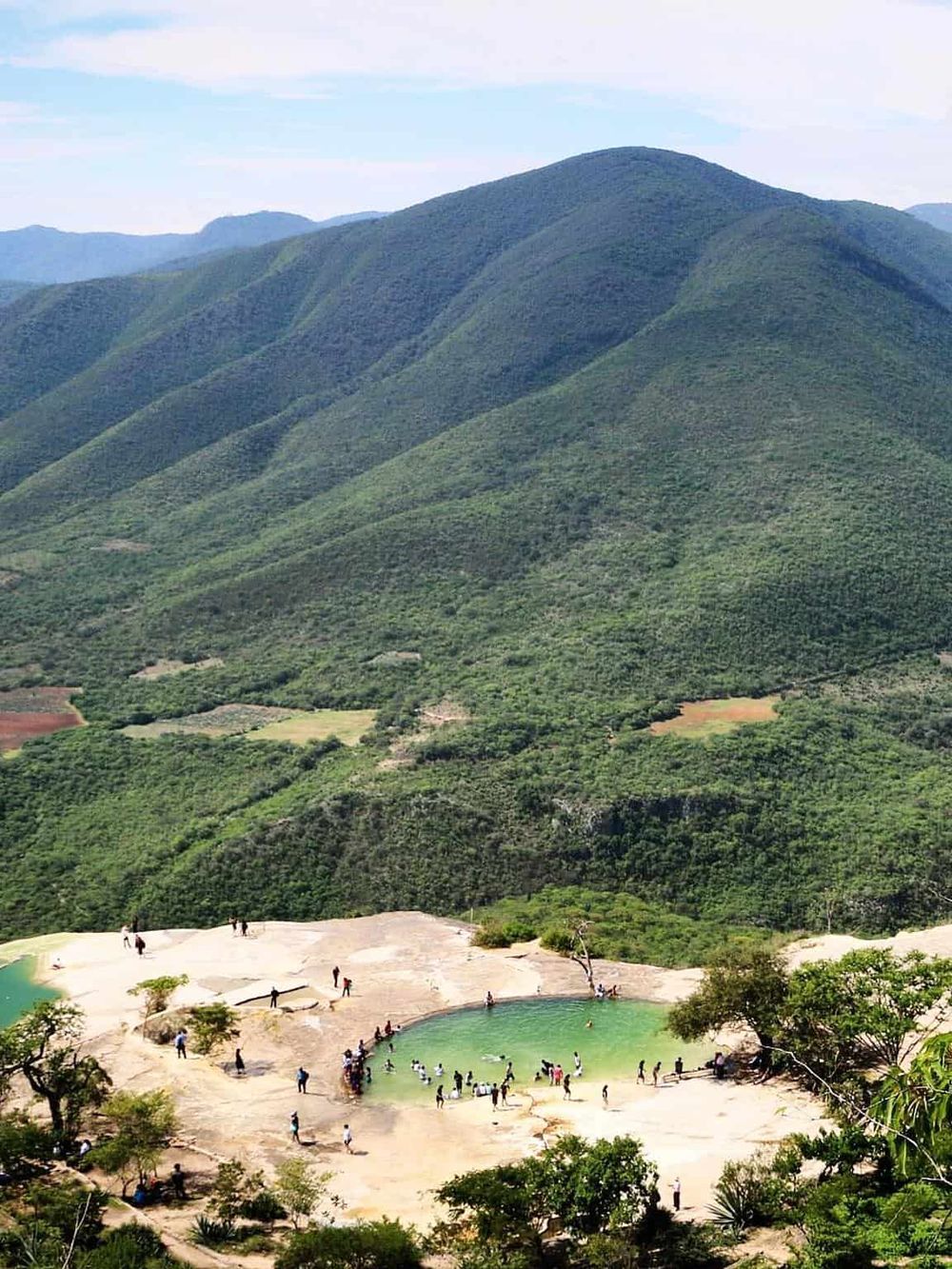 Scenic mountain landscape with lush greenery and a popular natural hot spring with visitors relaxing in the mineral pools.